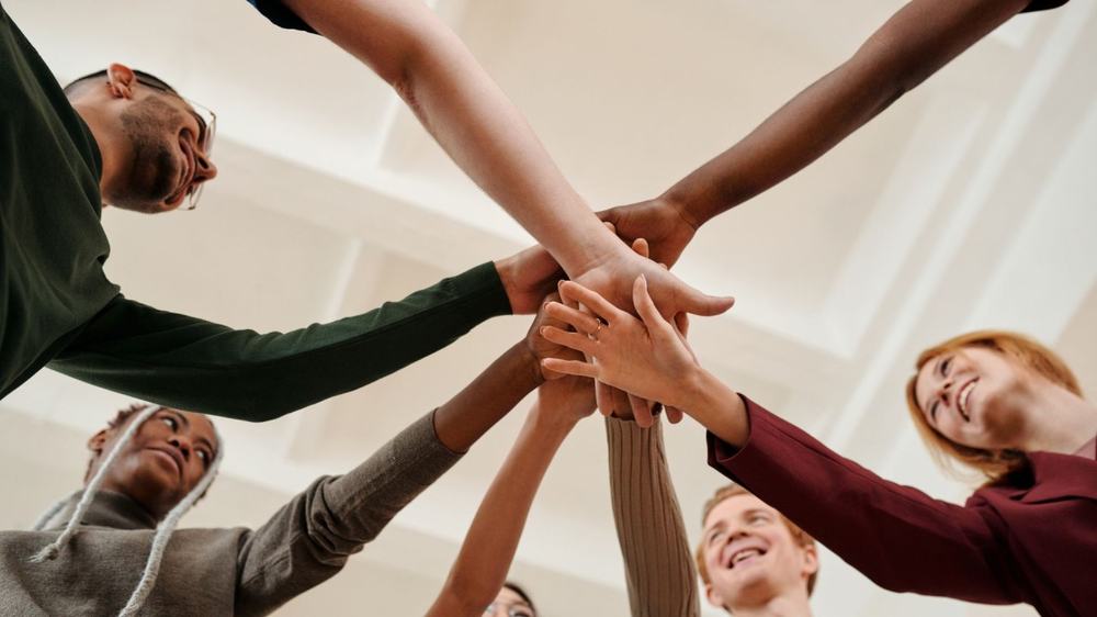 Diverse coworkers smiling as they stack their hands together in a circle, seen from below