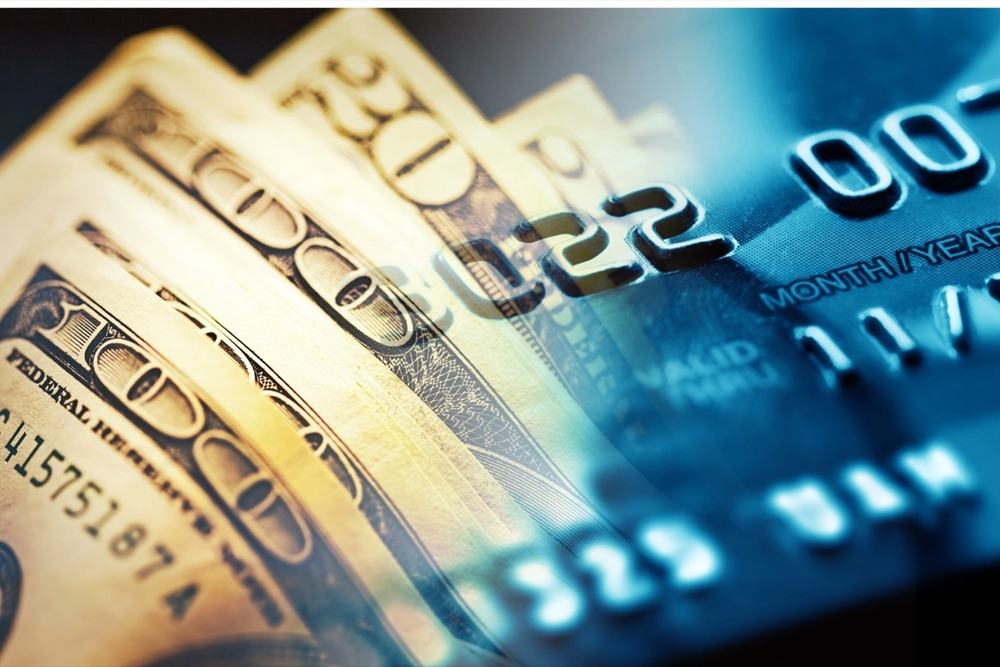Fanned US hundred-dollar bills blending into a close-up of a credit card