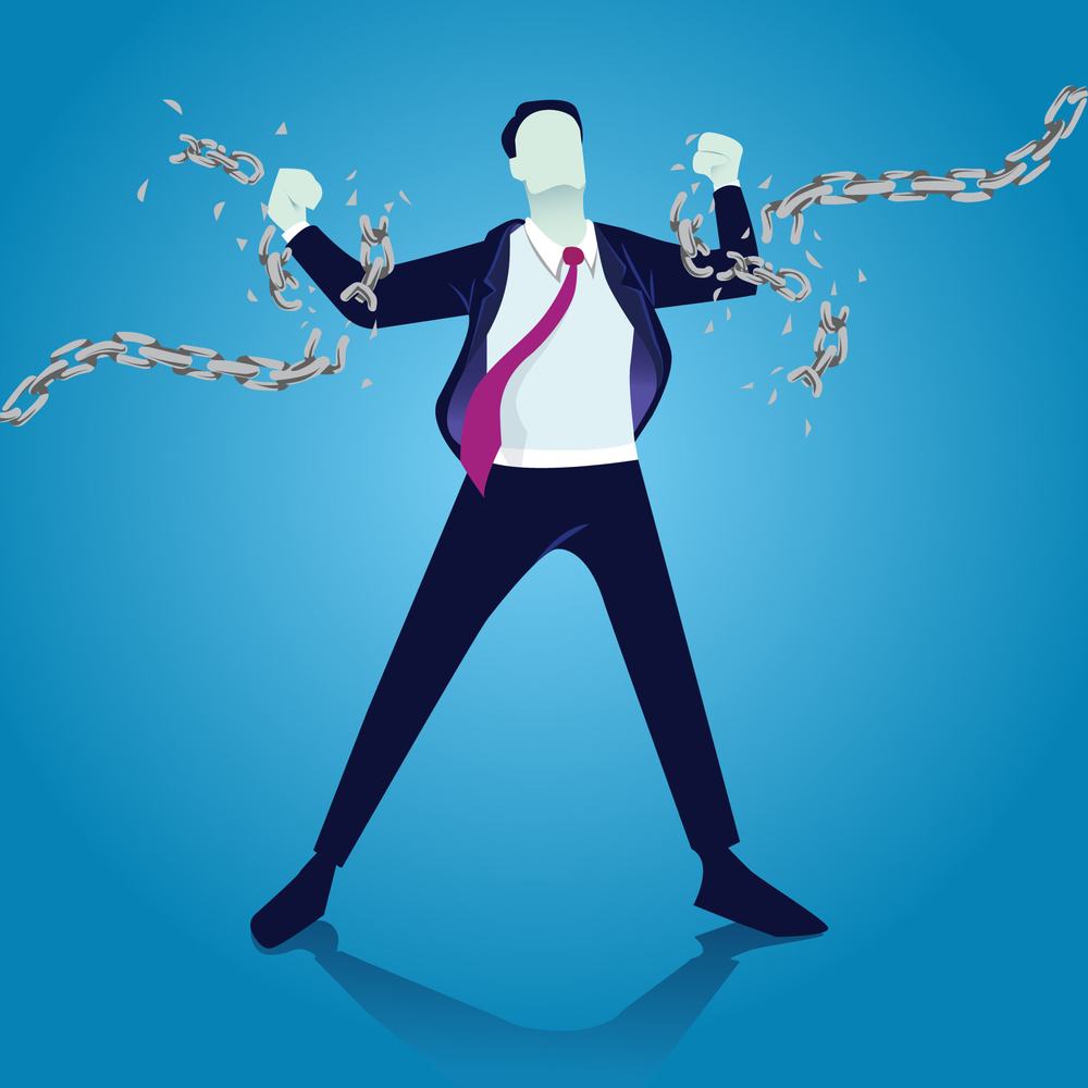 Businessman in a suit breaking the chains around his wrists, fists raised, against a blue background