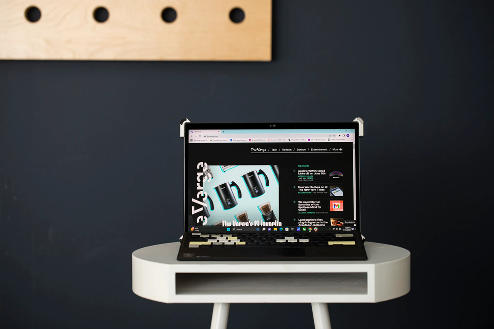 Tablet-style laptop showing The Verge homepage on a small white side table against a dark wall