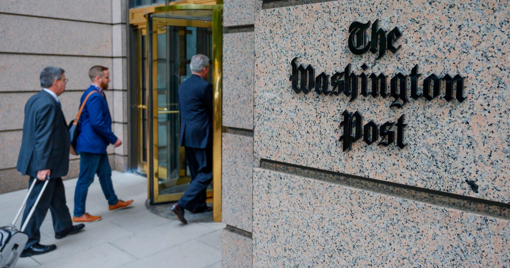People walking into The Washington Post building past its sign on a granite wall