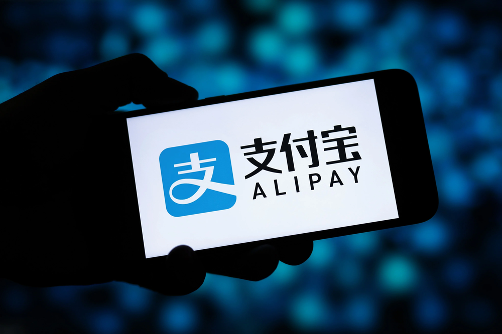 Hand holding a smartphone that shows the Alipay logo, Ant Group's payment app