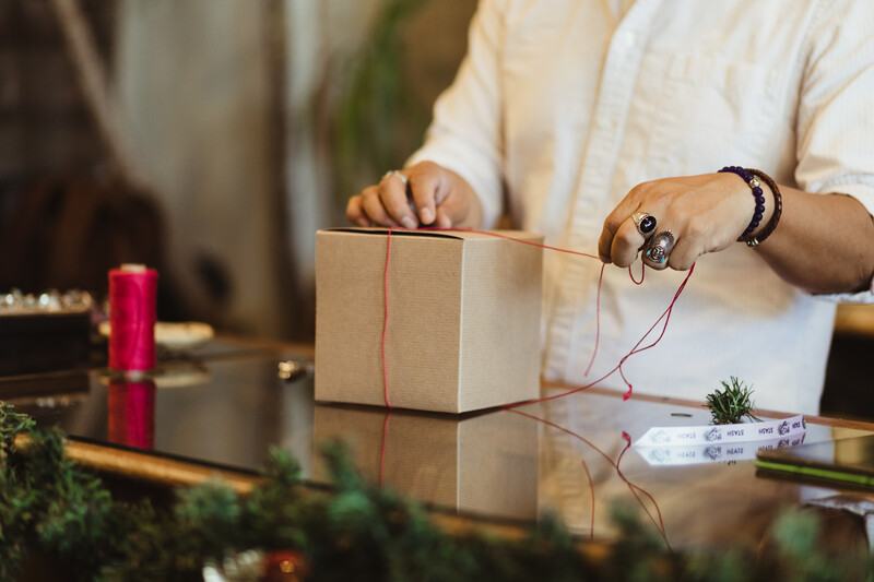 Person tying red string around a kraft gift box on a counter