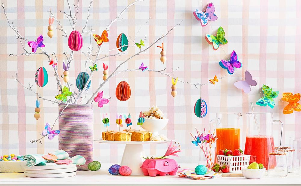 Easter table with paper eggs and butterflies hung on white branches, cakes, colorful drinks, strawberries and candy eggs