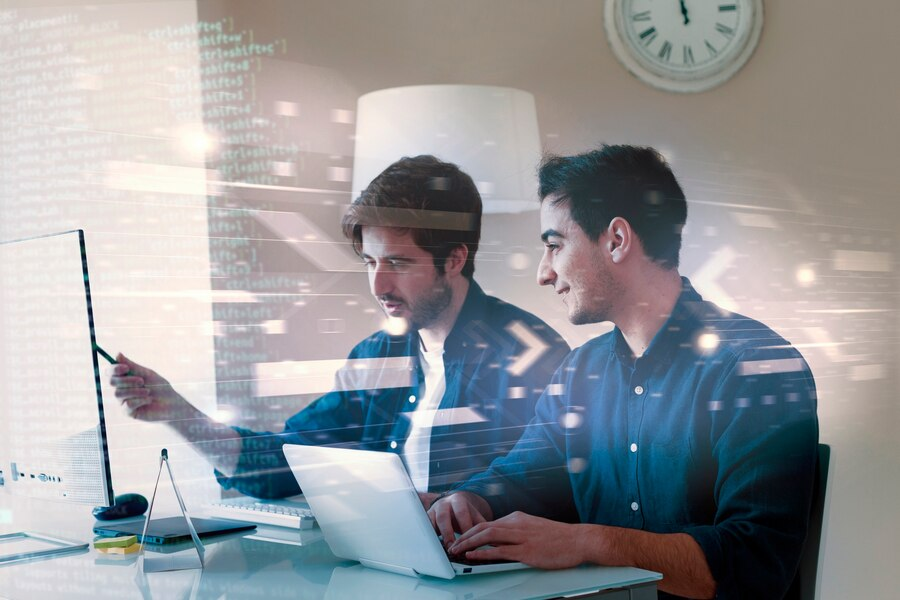 Two engineers reviewing code on a laptop and a screen in a bright office
