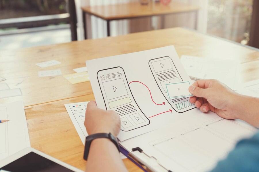 Hands arranging paper prototypes of app screens on a desk
