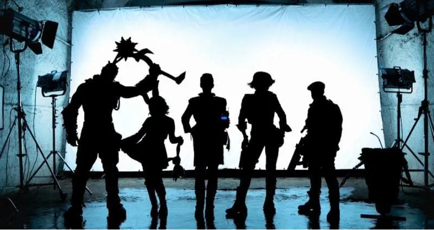 Silhouettes of five costumed figures posing before a backlit white screen on a film set, one holding a spiked prop overhead