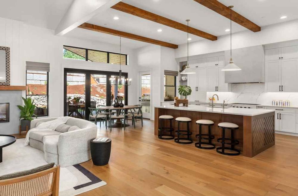 Bright open-plan home with oak floors, wooden ceiling beams, a kitchen island with stools and a gray sofa