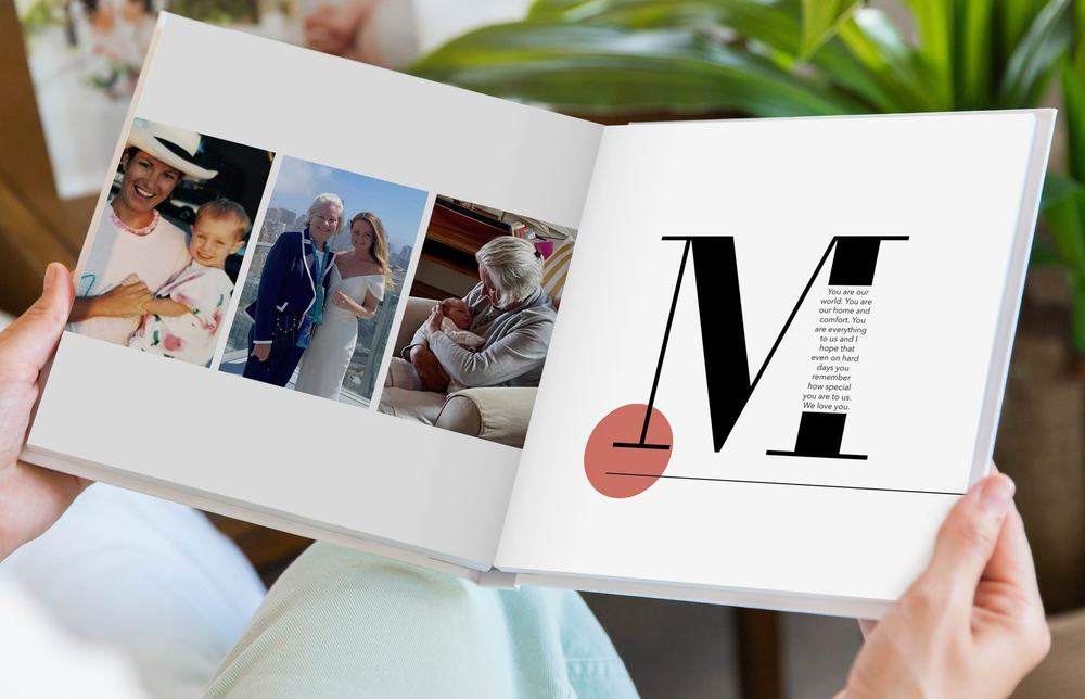 Hands holding an open photo book with family snapshots and a page with a large letter M and a loving message