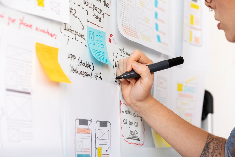 A designer sketching mobile app wireframes and sticky notes on a whiteboard