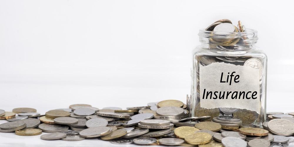 Glass jar labeled Life Insurance, filled with coins, with more coins spilled across the table
