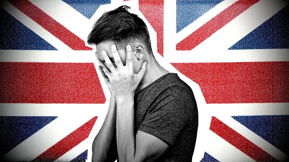 Young man covering his face with his hand in front of a British Union Jack flag