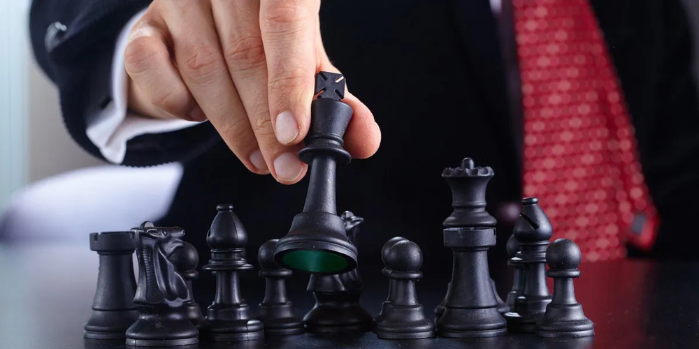 Businessman in a red tie moves a black chess piece forward from a row of pieces