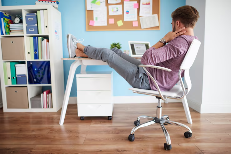 Man leaning back in an office chair with his feet up on a white desk, beside shelves and a pinboard