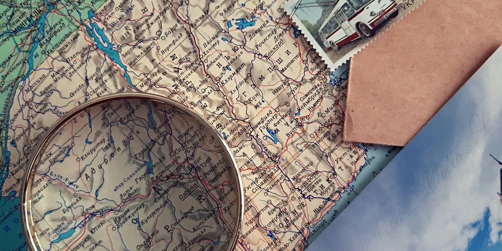 Magnifying glass over a Cyrillic-language road map, next to a postage stamp and an envelope