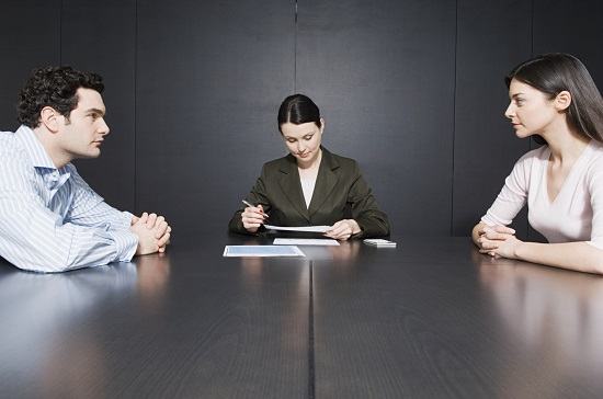 A mediator takes notes at a long table between a man and a woman seated apart, facing each other