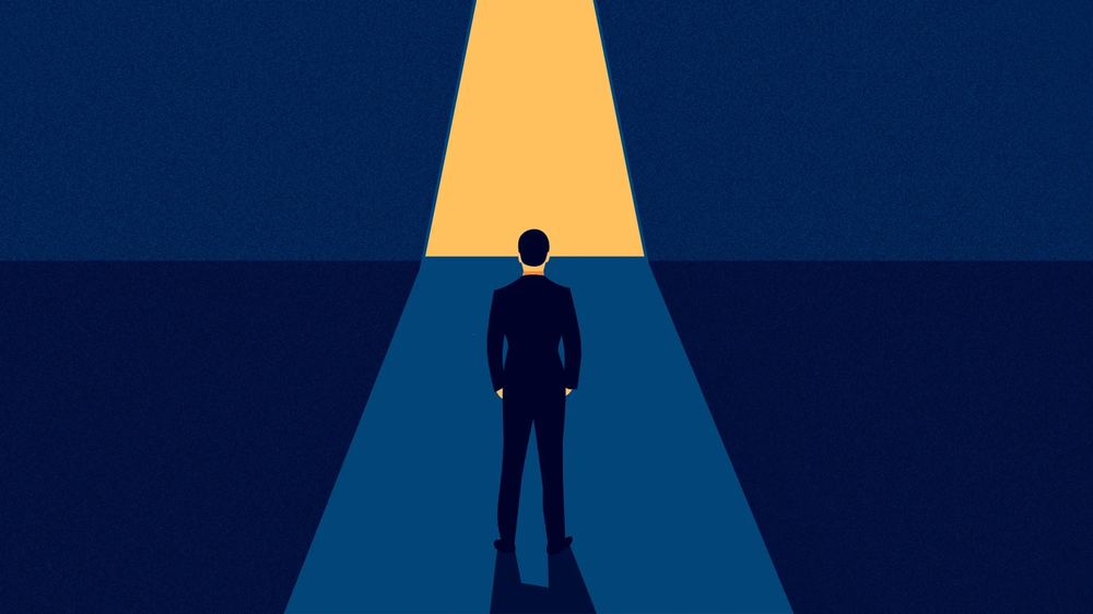 Silhouetted businessman stands at the start of a lit path leading toward a bright opening