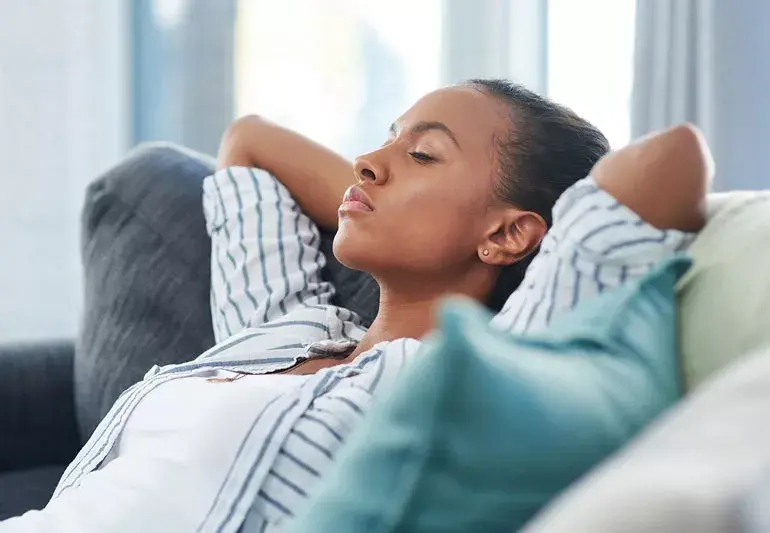 Woman resting on a couch with her eyes closed and her hands behind her head