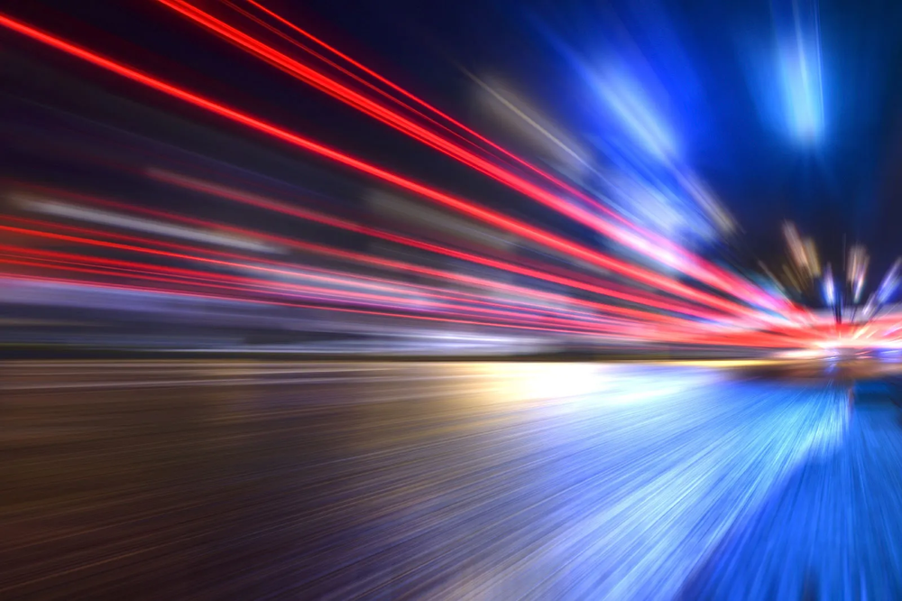 Long-exposure night road with red and blue light trails streaking past at speed