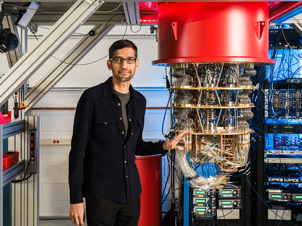 Sundar Pichai stands beside one of Google's quantum computers, a tiered rig of gold plates and wiring under a red casing